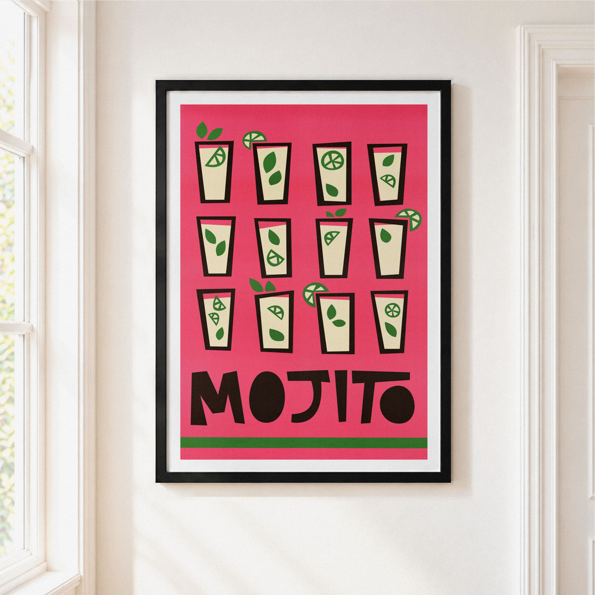 A framed Mojito cocktail art print hanging on a white wall next to a window. The print features a bright pink background with illustrations of mojito glasses, lime slices, mint leaves, and the word 'MOJITO' in bold black letters at the bottom.