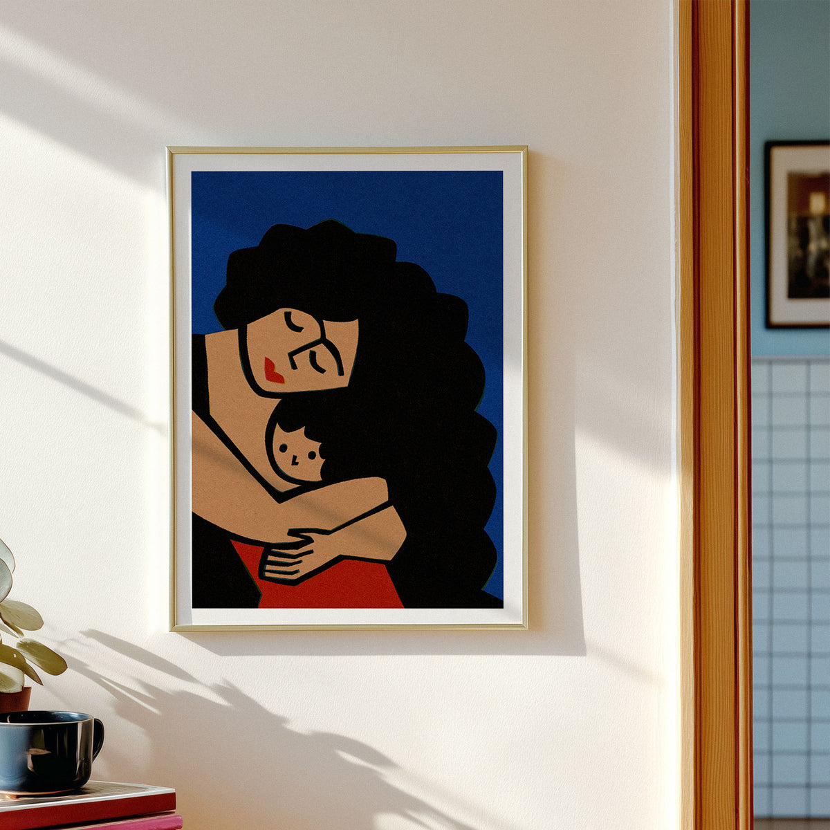 A framed art print featuring a stylized mother and child embrace in bold colors, hanging on a white wall in a sunlit room.