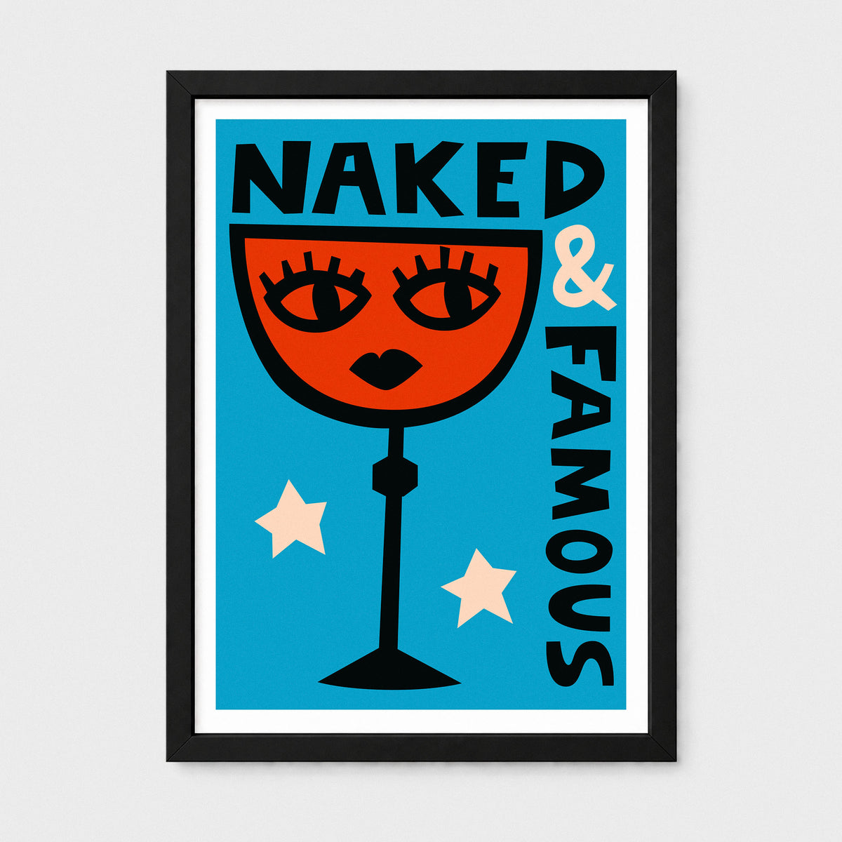 A framed art print featuring a retro-style illustration of a red cocktail glass with a female face, the text 'NAKED & FAMOUS' in black, and two cream stars on a bright blue background, shown in a black frame against a light gray wall.