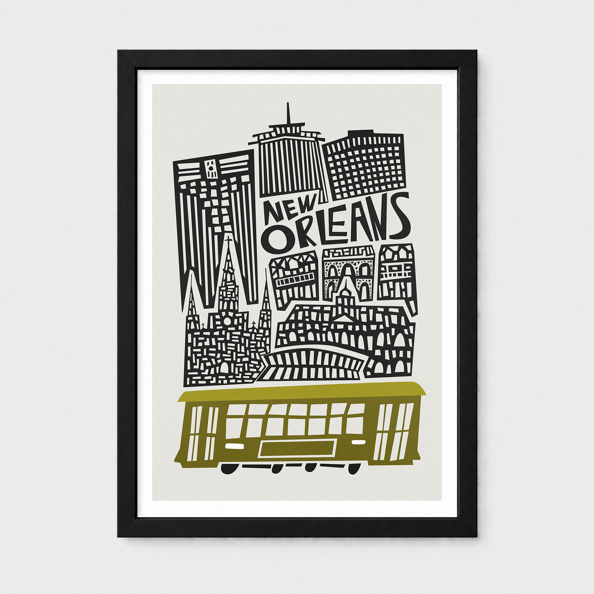 Framed New Orleans cityscape art print with black buildings, the words 'NEW ORLEANS,' and an olive-green streetcar on a light gray background, shown in a black frame against a light gray wall.