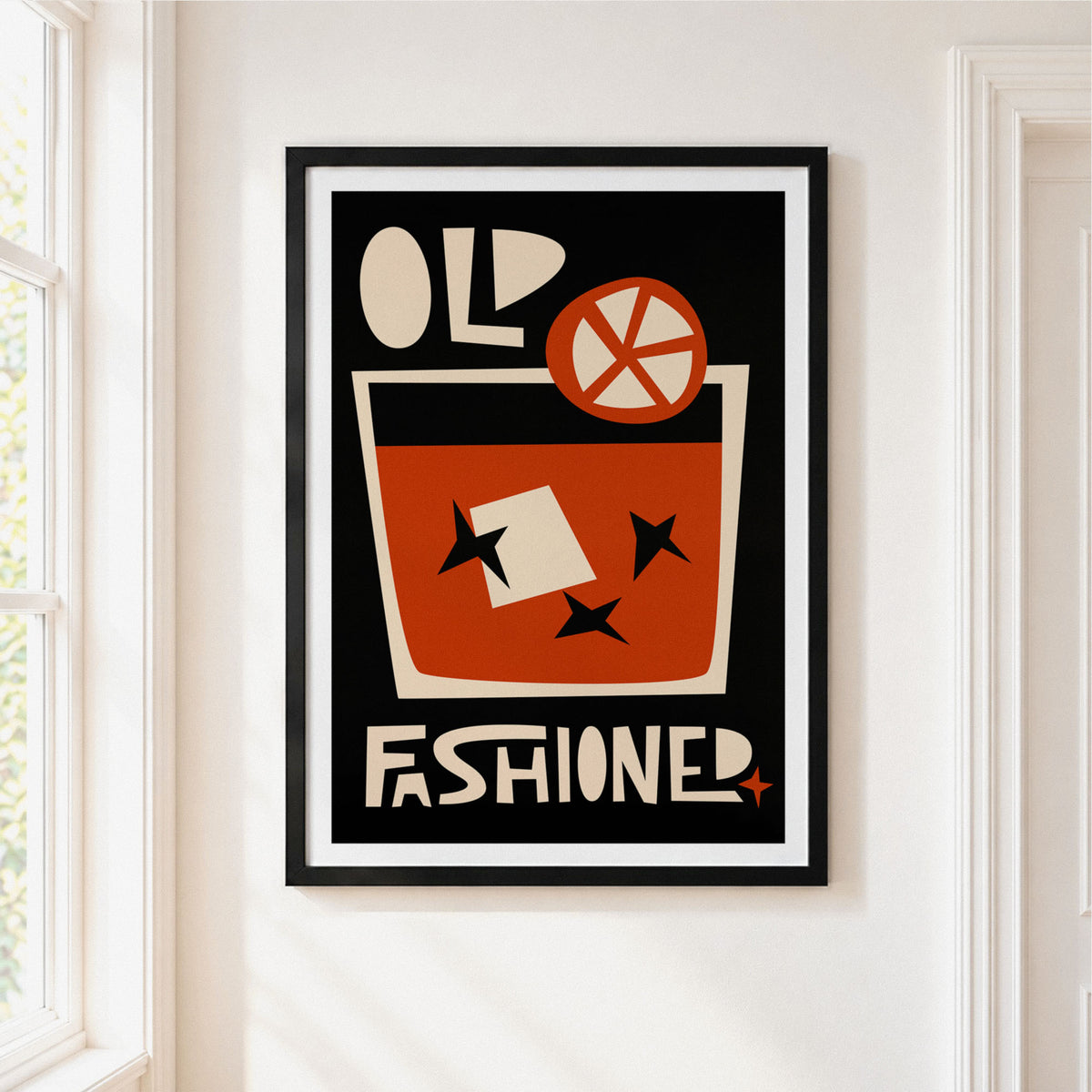 A framed vintage-style poster hanging on a white wall beside a window. The poster features a black background with cream and rust-orange graphic elements, including the words 'OLD FASHIONED' and a stylized drink illustration with a garnish.