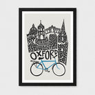 A framed art print featuring a stylized black-and-white illustration of Oxford landmarks above a blue bike on a light gray background, shown in a black frame with white matting.