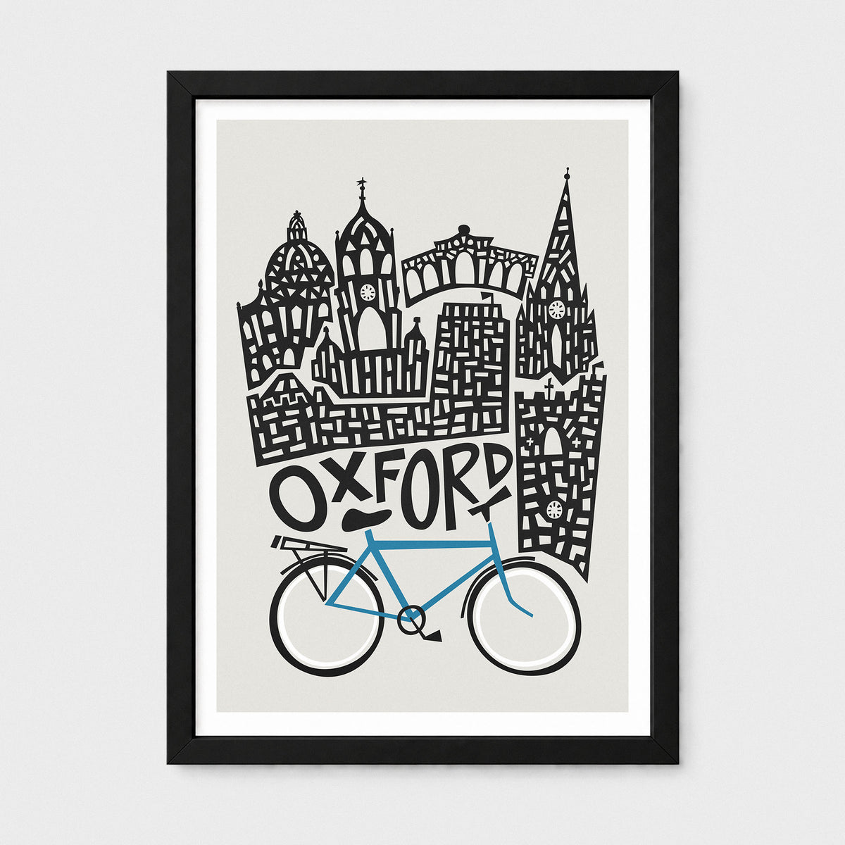 A framed art print featuring a stylized black-and-white illustration of Oxford landmarks above a blue bike on a light gray background, shown in a black frame with white matting.