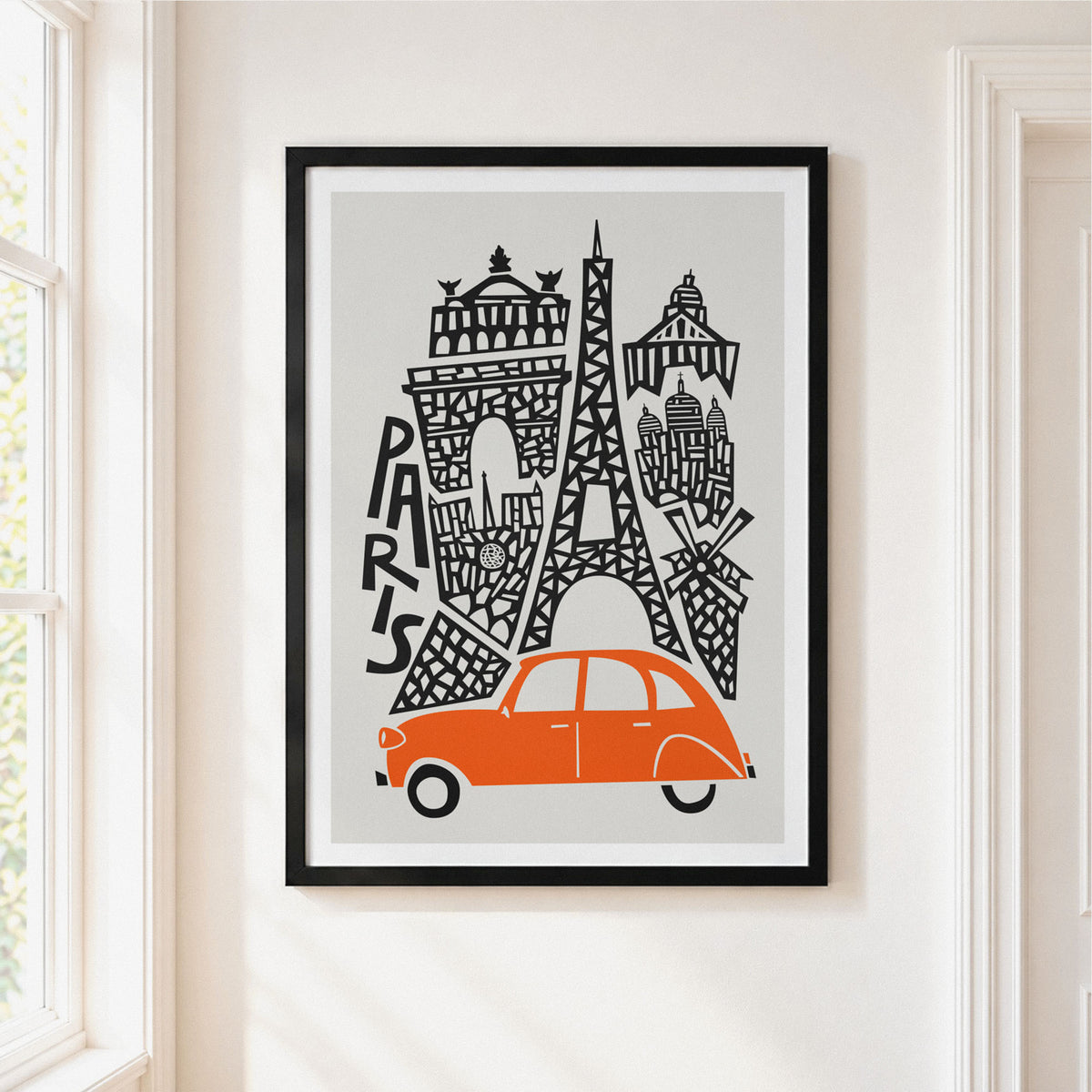 A framed art print featuring a stylized paris skyline with an orange car and black architectural details on a light gray background, hung on a cream-colored wall next to a window.