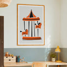 A framed art print of a Parisian carousel illustration hanging on a wall above a wooden desk in a modern room setting.