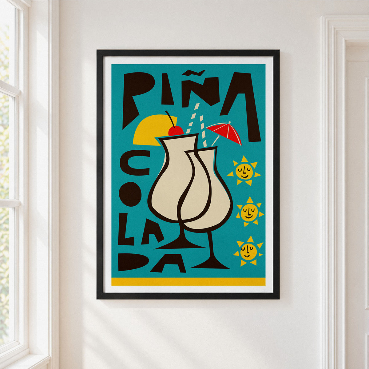 A framed art print featuring a retro-style illustration of two Pina Colada cocktails, displayed on a white wall next to a window.