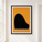 A framed minimalist art print of a black grand piano silhouette against a warm orange background, hanging on a white wall next to a window.