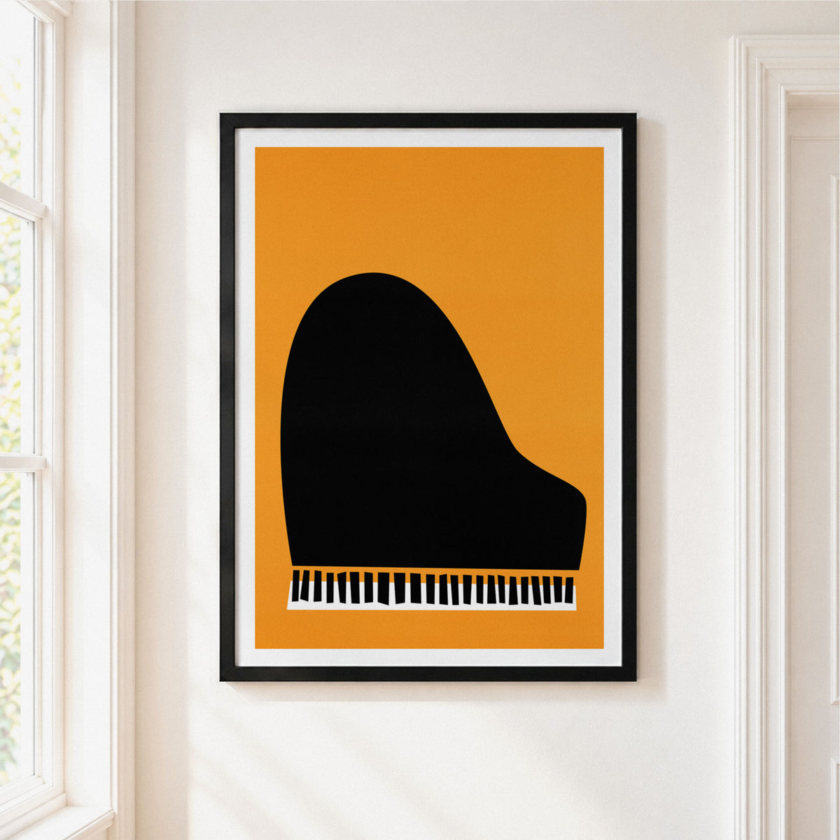 A framed minimalist art print of a black grand piano silhouette against a warm orange background, hanging on a white wall next to a window.