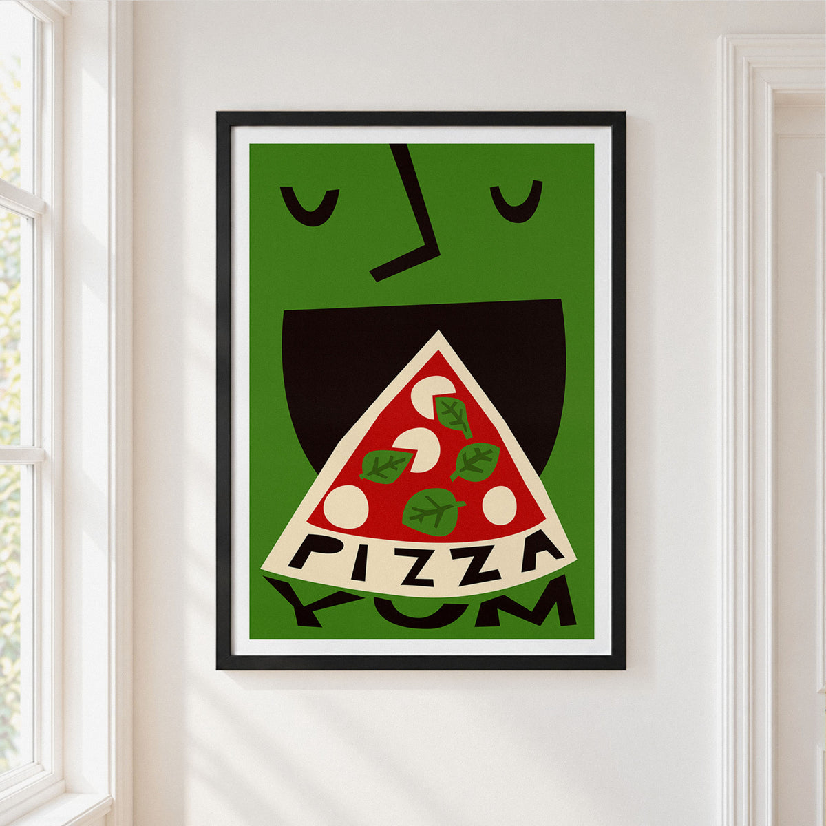 A framed art print featuring a stylized green face with black features and a slice of pizza in its mouth, hung on a white wall next to a window.