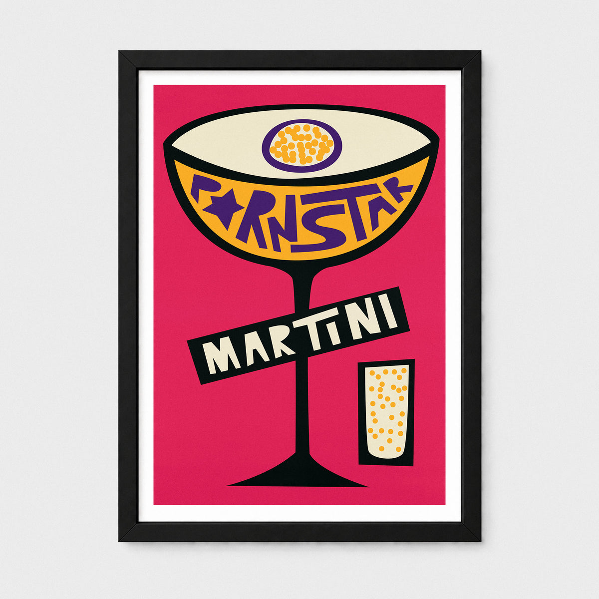A framed pop-art style print featuring a cocktail glass labeled 'MARTINI' on a bright pink background, shown against a light gray wall.