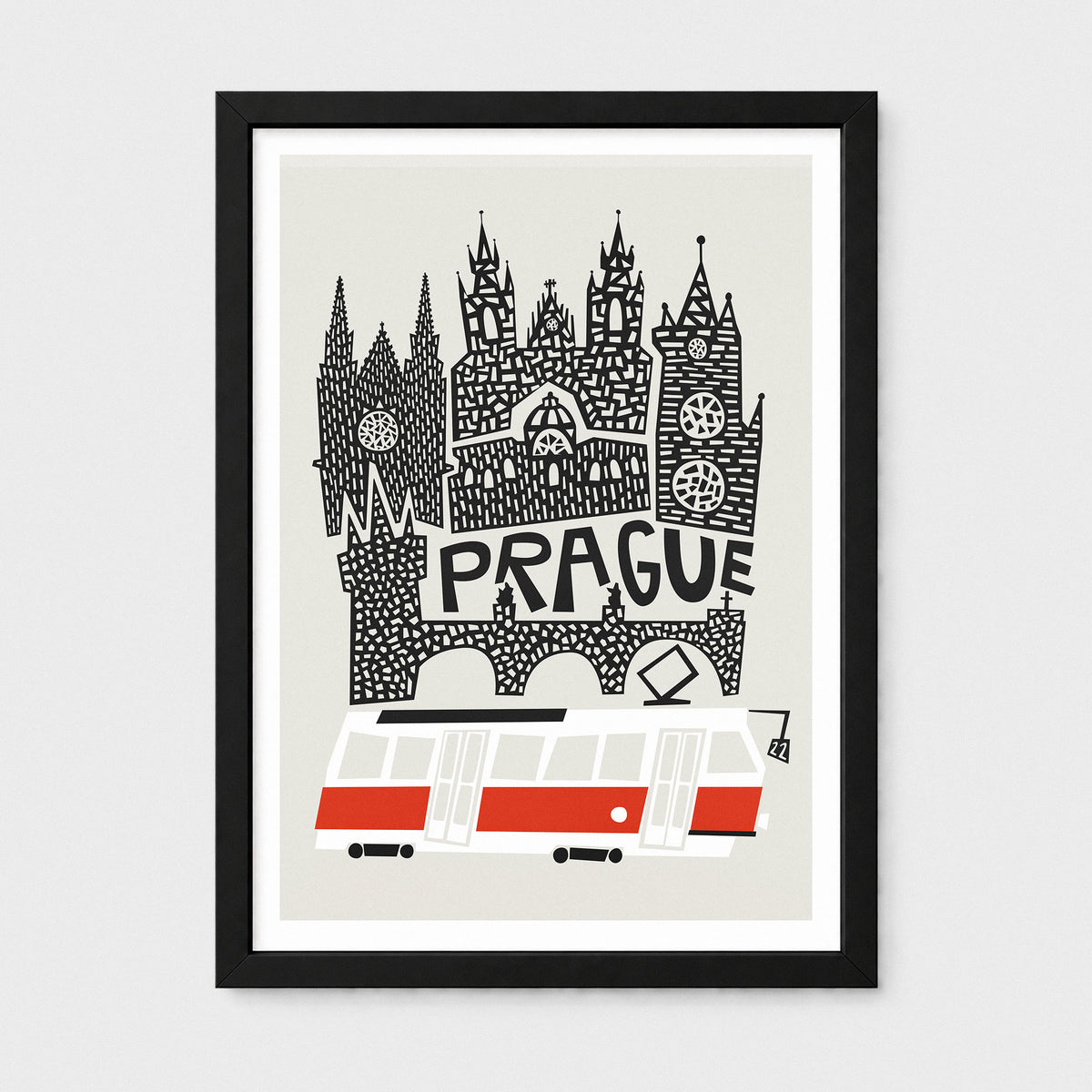 A framed travel art print of Prague, featuring a black and white hand-drawn illustration of the city's skyline and a red and white tram on a light beige background, enclosed in a black frame with a white mat.