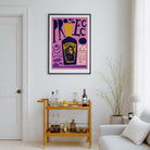 A framed pop-art print featuring a purple and pink background with a yellow bottle of prosecco illustration and stylized text, displayed on a white wall above a wooden bar cart in a modern living room setting.