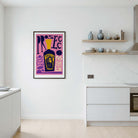 A framed art print featuring a purple and pink abstract design with a yellow bottle of prosecco illustration, displayed on a white wall in a modern kitchen setting.