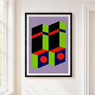 A framed abstract geometric art print featuring bold blocks of green, red, blue, and black on a lavender background, hung on a white wall next to a window.