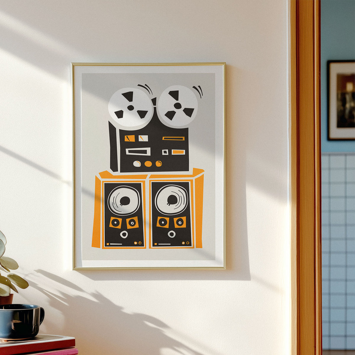 A framed abstract geometric art print hangs on a white wall in a sunlit room. The artwork features two stacked blue rectangles with orange diamond shapes, black centers, olive green circular forms, and pale pink vertical ovals.