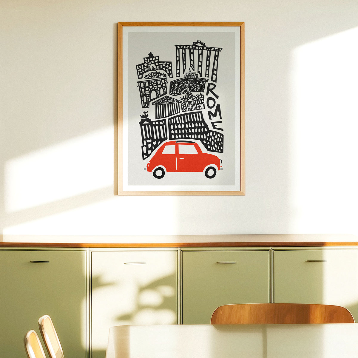 A framed art print featuring a stylized black and white illustration of Rome with a bright red car, hanging on a light beige wall above a green cabinet in a modern room setting.