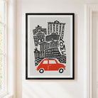 A framed art print featuring a stylized black line drawing of Rome with a red car at the bottom, displayed on a light beige wall in a doorway.