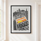 Framed San Francisco cityscape art print hanging on a white wall, featuring black line art of buildings and a bright orange and yellow tram on a light gray background.