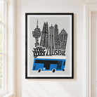 A framed art print featuring a stylized black and white Seoul skyline with a blue bus, hanging on a light beige wall in a bright room.