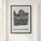 A framed art print featuring a black and white hand-drawn illustration of Sheffield landmarks and a white tram with orange and blue stripes, hanging on a cream-colored wall next to a window.