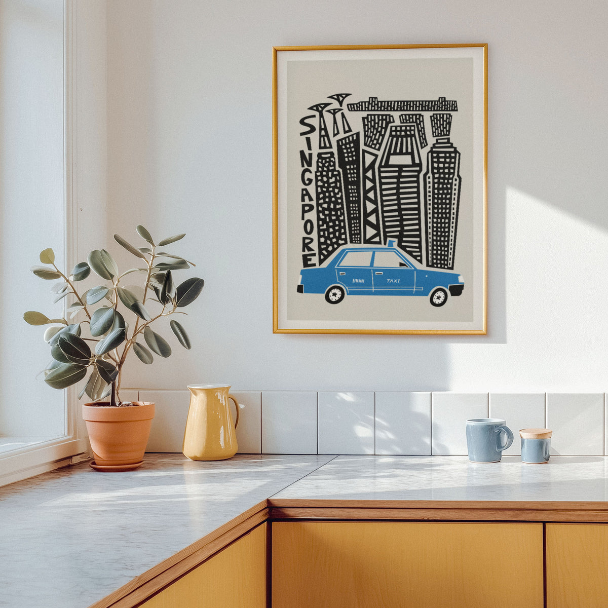 A framed art print featuring a stylized black and white cityscape with a blue car and the word 'SINGAPORE' on the wall above a kitchen counter. The print is shown in a real interior setting with a potted plant, yellow pitcher, and blue mugs.