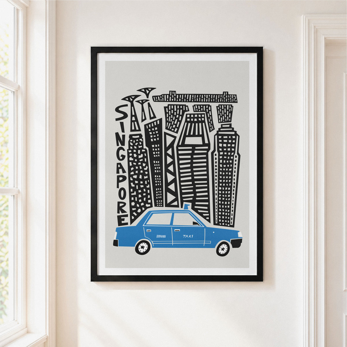 A framed art print featuring a stylized black and white skyline with the word 'SINGAPORE' and a blue taxi at the bottom, hanging on a light beige wall next to a window.