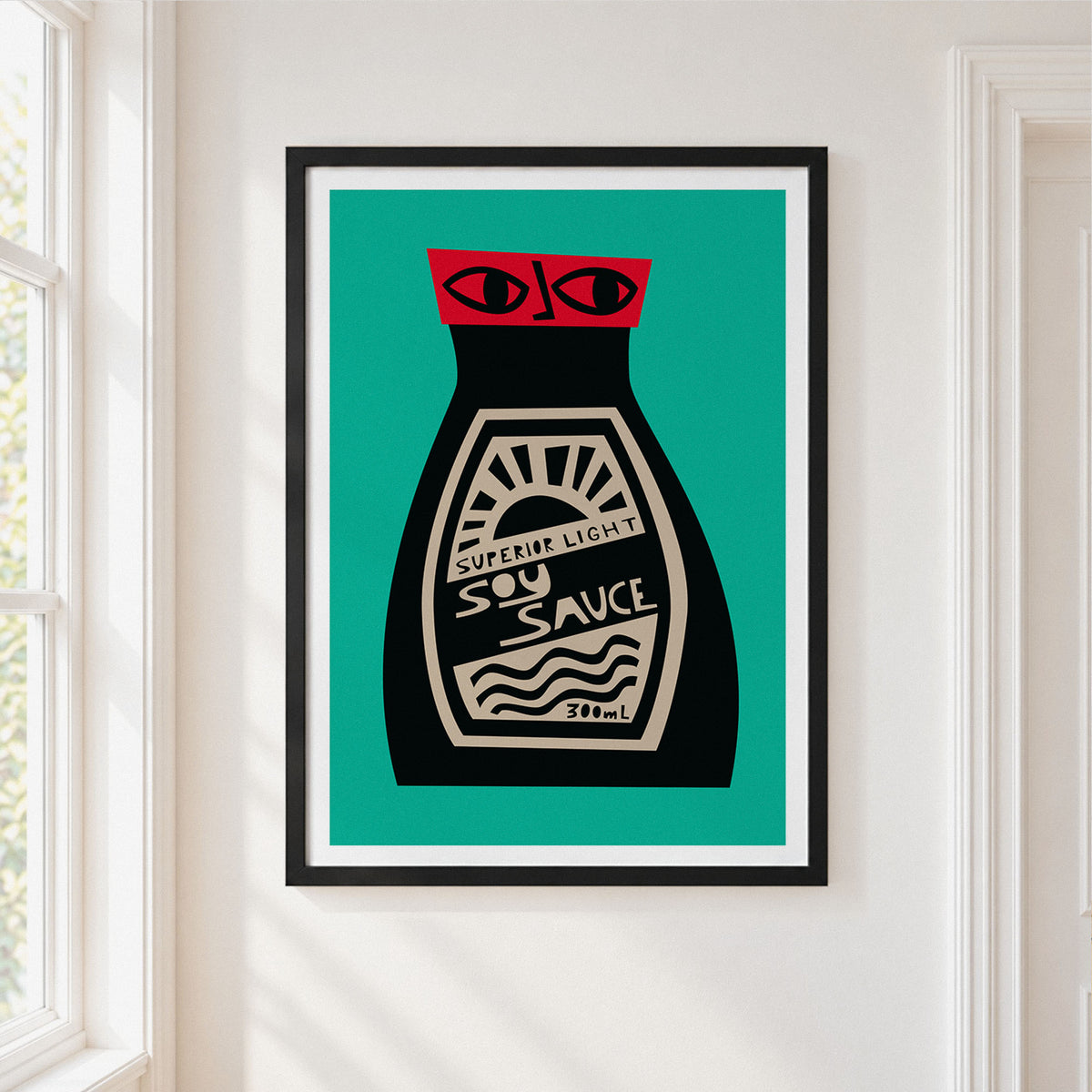A framed art print featuring a stylized soy sauce bottle with a red cap and cream label on a teal background, hung on a white wall next to a window.