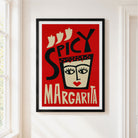 A framed art print featuring a stylized red poster with the words 'SPICY MARGARITA' and a face illustration, hung on a white wall next to a window.