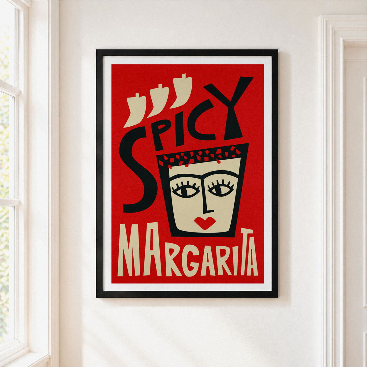 A framed art print featuring a stylized red poster with the words 'SPICY MARGARITA' and a face illustration, hung on a white wall next to a window.