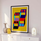 Colorful geometric abstract art print in a black frame on a white wall.