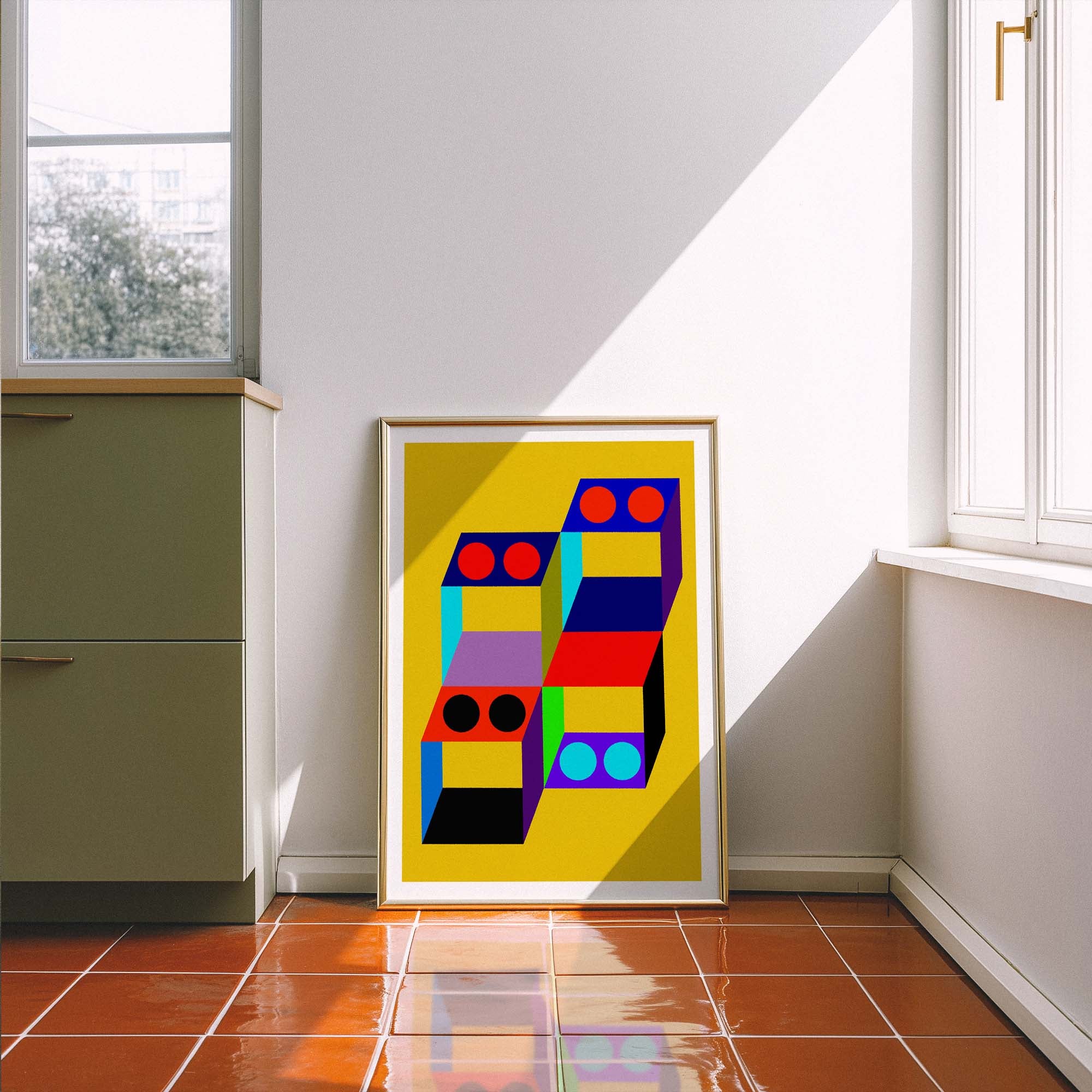 Colorful abstract art print in a gold frame on a white wall with a window and cabinet in the background.