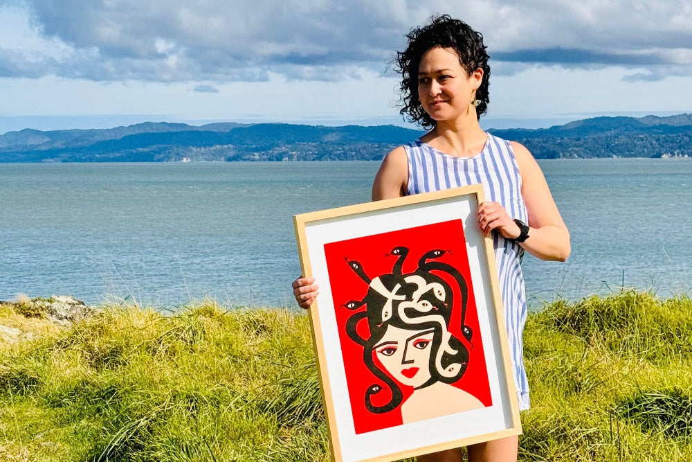 Suumin holding Medusa print with a scenic backdrop.