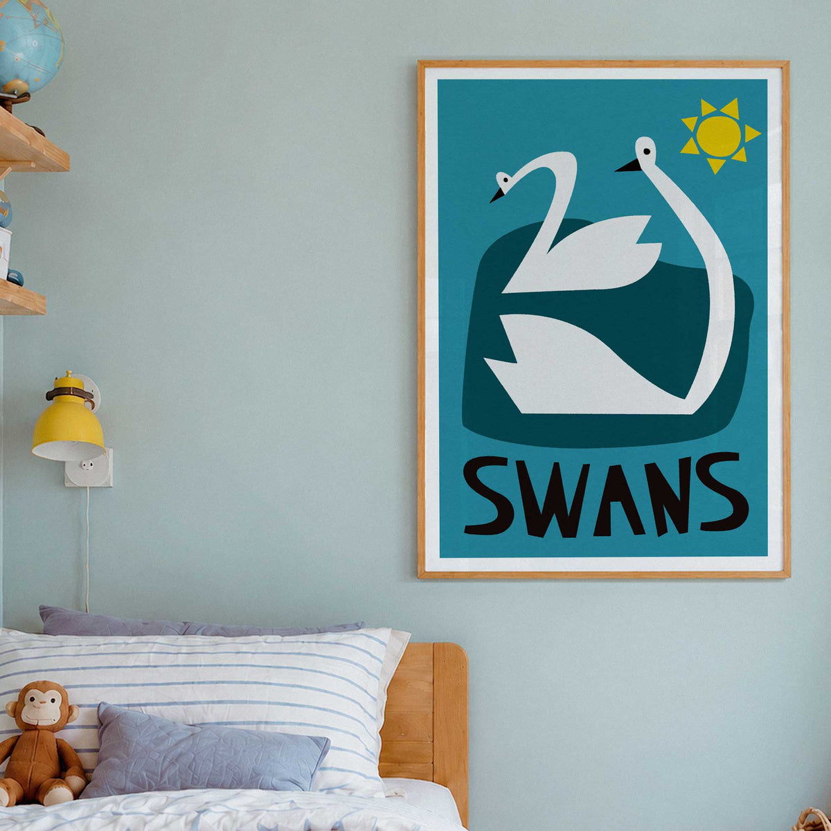 A framed wall art print featuring two white swans and the word “SWANS” in black, hanging on a light blue-gray wall above a bed in a styled bedroom.