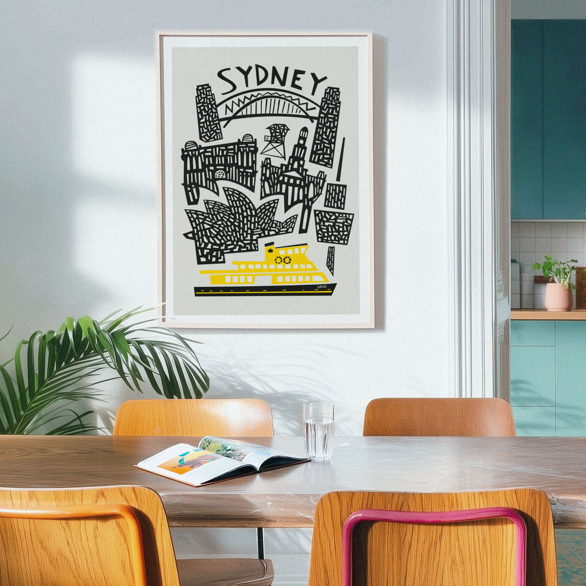 A framed Sydney travel art print featuring black line drawings of landmarks and a bright yellow ferry on a light gray background, hanging on a white wall above a wooden dining table with chairs in a modern kitchen setting.