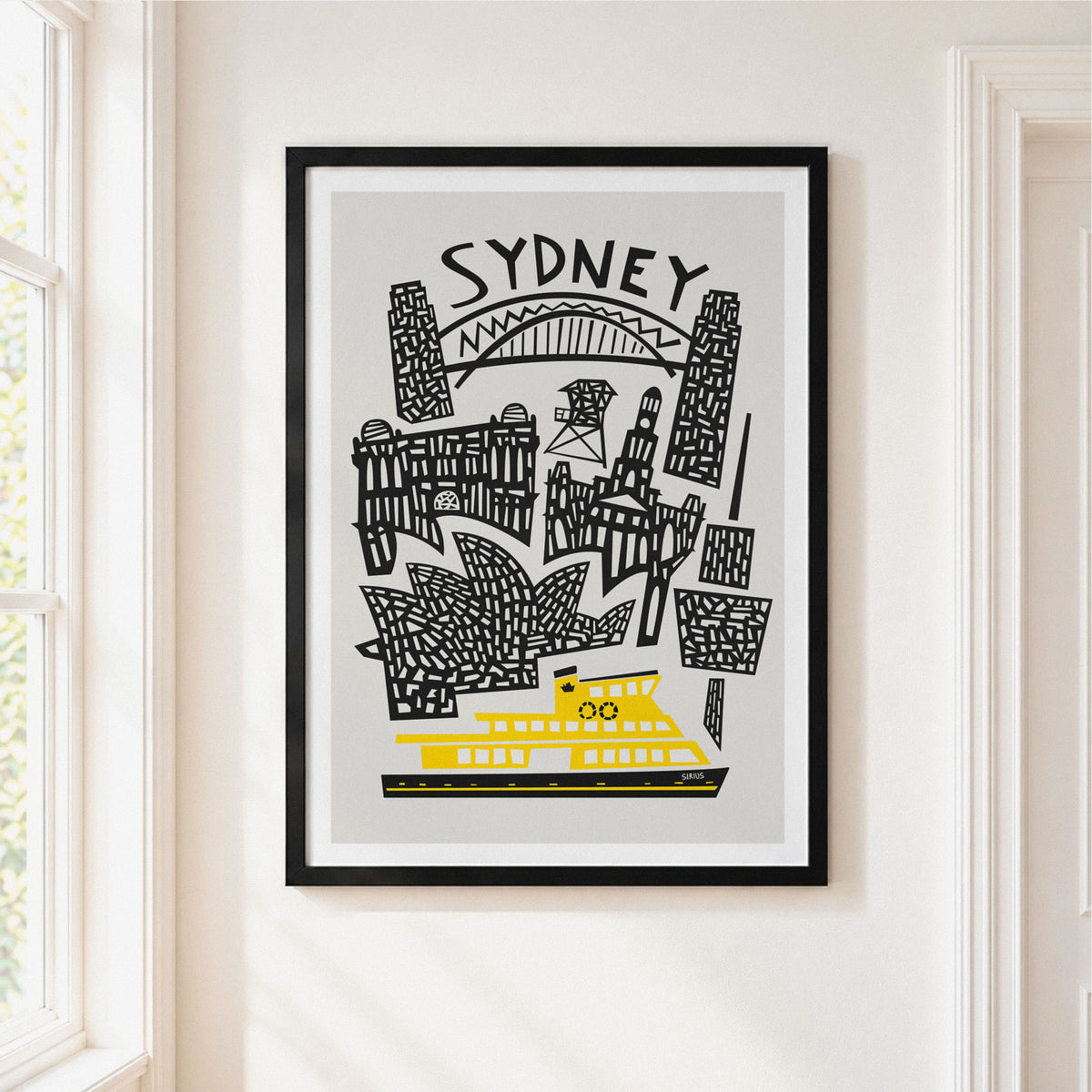 A framed Sydney art print hanging on a white wall next to a window. The print features black hand-drawn illustrations of Sydney landmarks, including the Sydney Opera House, Sydney Harbour Bridge, and the Sydney Ferry, on a light gray background with the word 'SYDNEY' at the top.