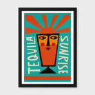 A framed art print featuring a stylized graphic illustration of a tequila glass with a face, surrounded by radiating orange rays and the words 'TEQUILA' and 'SUNRISE' on a teal background, shown in a black frame against a light gray wall.