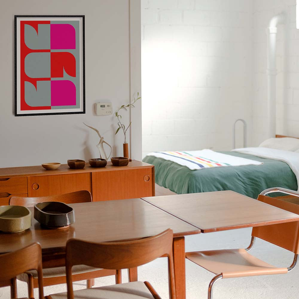 Dining area with wooden table and chairs, bed in the background, and colorful abstract art on the wall.