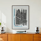 A framed black and white Tokyo cityscape art print with light blue accents hangs on a white wall above a wooden credenza, flanked by two white speakers and a vinyl record player.