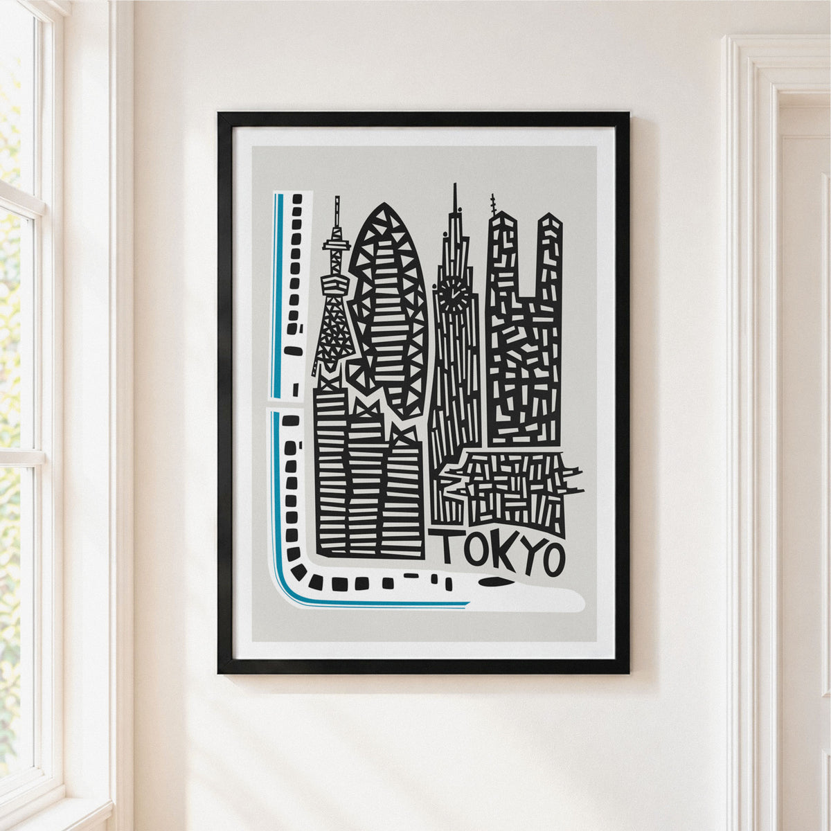 A framed minimalist art print of the Tokyo skyline, featuring black and white architectural illustrations with a light blue route line and the word 'TOKYO' at the bottom. The print is housed in a black frame and displayed on a warm beige wall next to a window.