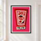 A framed art print featuring a retro ketchup bottle illustration with the words 'TOMATO KETCHUP' on a bright pink background, hung on a white wall next to a window.