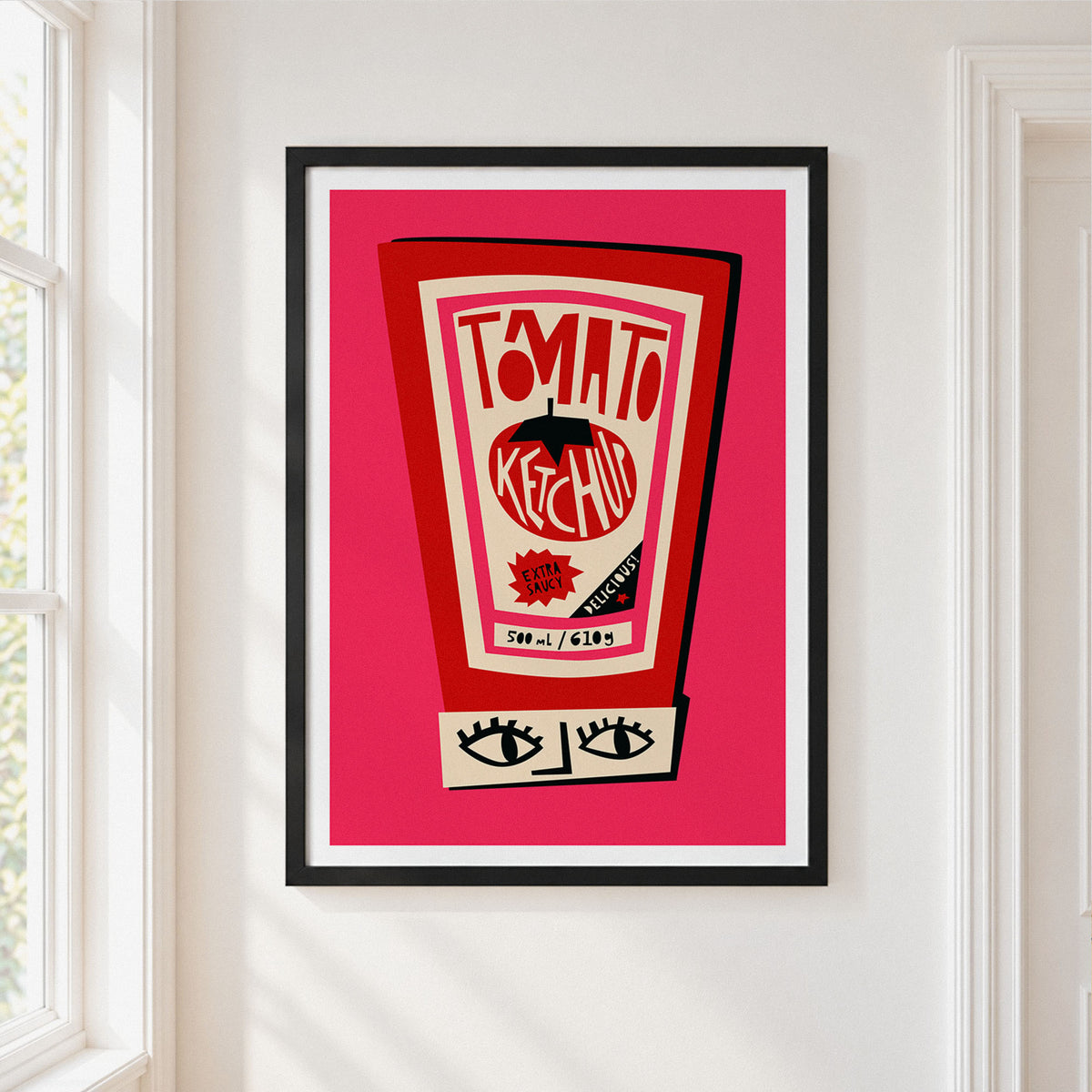 A framed art print featuring a retro ketchup bottle illustration with the words 'TOMATO KETCHUP' on a bright pink background, hung on a white wall next to a window.