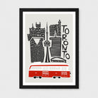 Framed Toronto cityscape wall art print with black buildings and text, a red trolleybus at the bottom, shown in a black frame against a light gray background.