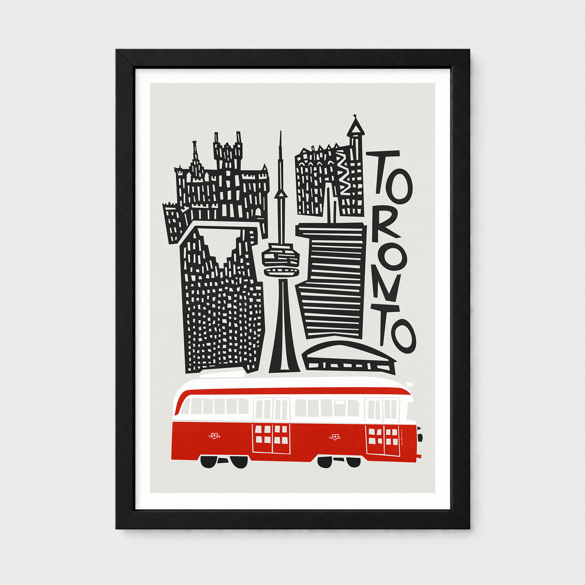 Framed Toronto cityscape wall art print with black buildings and text, a red trolleybus at the bottom, shown in a black frame against a light gray background.