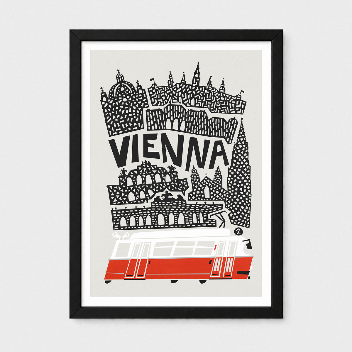 A framed art print featuring a stylized black and white map illustration of Vienna with the word 'VIENNA' in bold letters and a red and white tram at the bottom, shown against a light gray background.