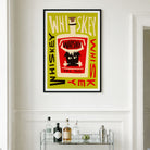 A framed art print featuring a stylized whiskey bottle illustration with the word 'Whiskey' repeated around it, hanging on a white wall above a glass bar cart with bottles and glasses.
