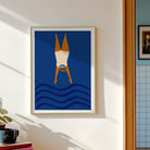 A framed art print featuring a stylized figure diving headfirst into blue waves, hanging on a white wall in a sunlit room.