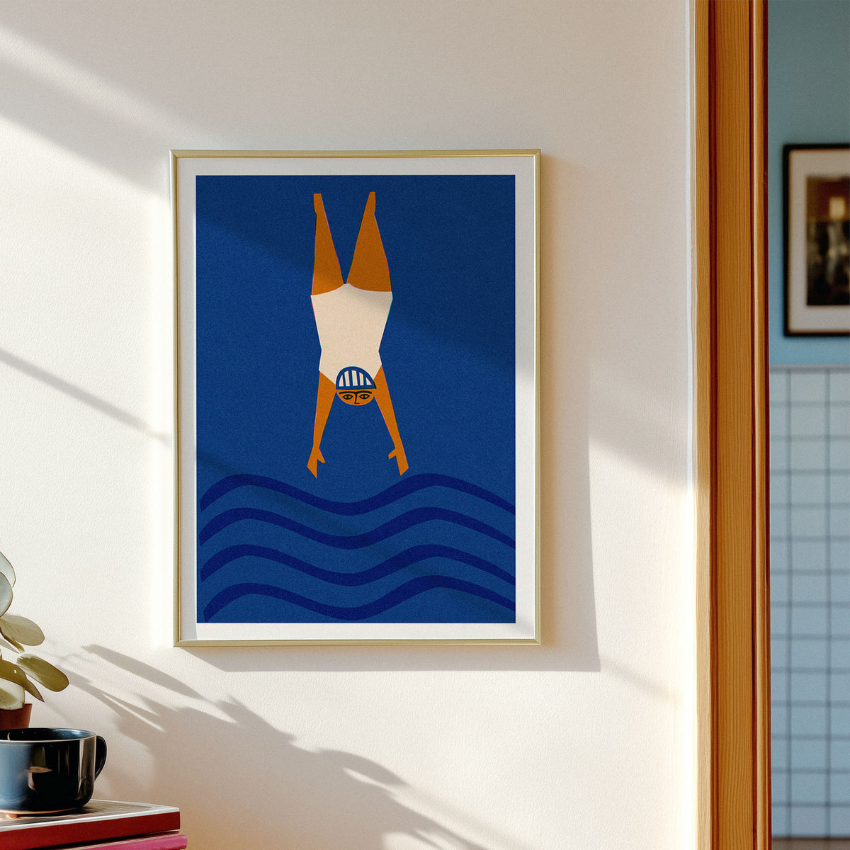 A framed art print featuring a stylized figure diving headfirst into blue waves, hanging on a white wall in a sunlit room.