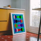 Colorful abstract art print in a white frame on a red tiled floor.