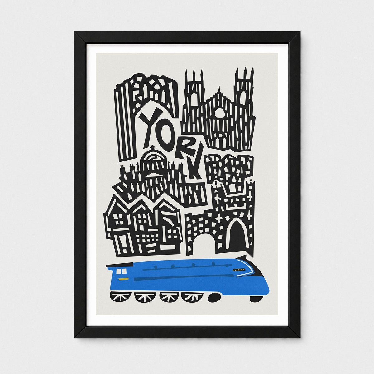 A framed art print featuring a stylized black and white illustration of York's skyline with the word 'YORK' integrated into the architecture, and a blue train at the bottom. The print is mounted with a white mat inside a black frame, shown against a light gray background.