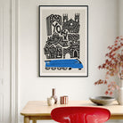 A framed art print featuring a stylized black and white illustration of York with a blue train, hanging on a light gray wall above a wooden table with decorative vases, a bowl, and a red chair.